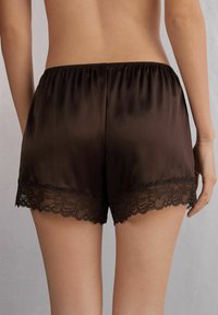 Bruna satinshorts med en mjuk, slät textur. Har en scallop-mönstrad svart spetskant vid fållen. Elastisk midja ger en bekväm passform.