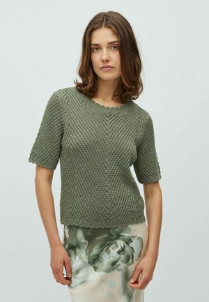 Olívazöld, rövid ujjú kötött pulóver texturált mintával, kerek nyakkivágással és fodros szegéllyel, virágmintás szoknyával párosítva.