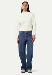 Kermainen ribbipaita, jossa on korkea kaulus ja lyhennetty malli, yhdistettynä rentoihin sinisiin farkkuihin ja harmaisiin lenkkareihin. Yksinkertainen, rento asu.