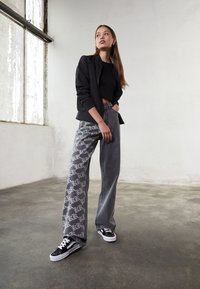 Løse grå bukser med et subtilt lys grått mønster, kombinert med en svart crop top og en svart bomberjakke, båret med svarte sneakers.