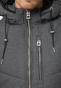 Gray insulated jacket featuring a textured fabric, silver zipper hardware, drawstring hood, and front pocket.