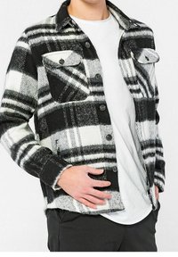 Svart och vit rutigt flanellskjorta med två bröstfickor, knappstängning och mjuk textur. Rundad nederkant och knäppta ärmslut.