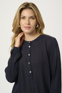 Blouse à manches longues bleu marine avec un col rond, dotée d'une patte de boutonnage et d'un tissu texturé. Des boutons argentés apportent un contraste.