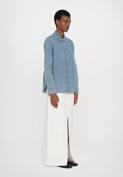 Denim button-up shirt in light blue, featuring a classic collar and long sleeves. Paired with a white maxi skirt with a front slit.