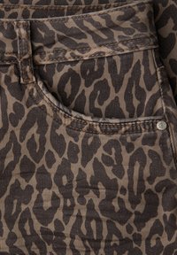 Lähikuva ruskeasta ja mustasta leopardikuvioisesta farkkukankaasta, jossa on etutasku ja vyölenkki, yksityiskohtaiset ompeleet ja metallinen niitti.