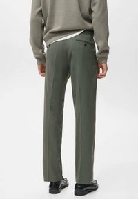 Pantalones formales verdes con un corte ajustado, que presentan una textura suave, un bolsillo trasero único y detalles de pliegues sutiles, combinados con zapatos negros.