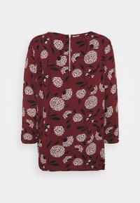 Tunika bordeaux con motivo floreale bianco e foglie nere. Caratterizzata da maniche lunghe e chiusura con zip sul retro. Tessuto morbido.