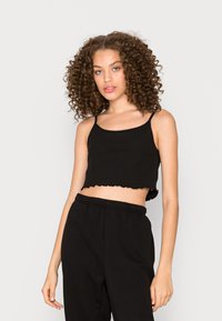 Top cropped preto com detalhes em nervuras, alças finas e barra ondulada. Combinado com calças pretas de cintura elástica. Textura suave, design ajustado.