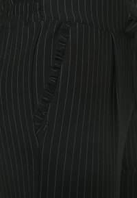 Černé kalhoty s jemným proužkem, vybavené texturovaným elastickým pasem a řaseným detailem kapsy. Obsahují malou značkovou nálepku "ONLY".