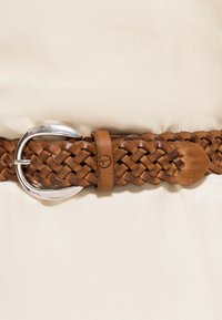 Splątany brązowy pasek ze skóry z metalową, srebrną klamrą, charakteryzujący się gładkim wykończeniem oraz subtelnym, wytłoczonym logo na skórzanym pasku.