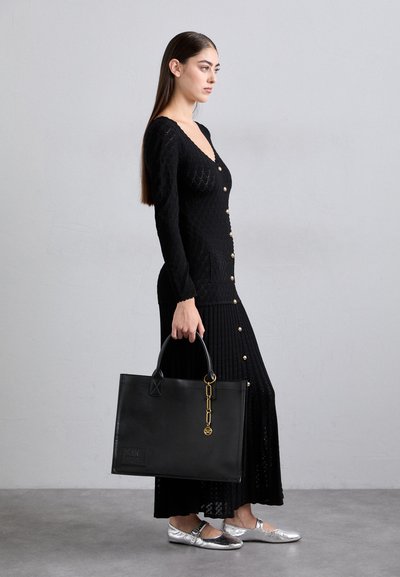 Zwarte gebreide jurk met knoopdetails, gecombineerd met een zwarte leren tas met een gouden kettingaccent en zilveren platte schoenen.