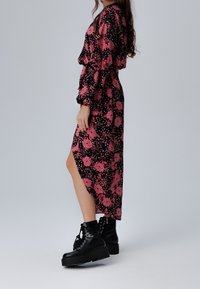 Lång svart klänning med rosa blommönster, puffärmar och en högt skuren slits. I kombination med kraftiga svarta snörstövlar.