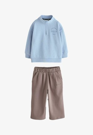 Lyseblå langærmet pullover med halv lynlås og brune elastiske vidde-bukser, begge med små tekst logo detaljer.