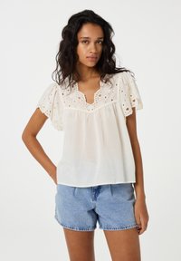 Witte blouse met borduursels en geschulpte mouwen, met een V-hals en een vloeiende pasvorm. Gecombineerd met lichtblauwe denim shorts.