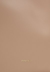 Blush pink synthetic leather bag with a smooth texture. Features gold "ANNA FIELD" logo at the bottom. Simple, rectangular design.