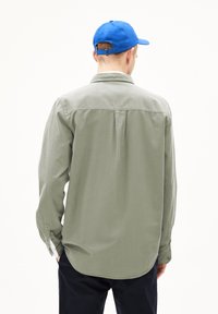 Lichtgroene overhemd met lange mouwen en een button-down kraag, met een yoke en plooien aan de achterkant. Gecombineerd met een blauwe pet.