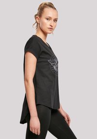 Svart t-skjorte med kort erm og buetkant, med et sølv Wonder Woman-logo og stjernemønster på forsiden. Mykt bomullsmateriale.