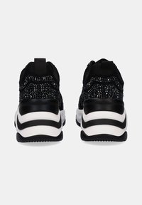 Zapatillas negras con un upper texturizado que presenta detalles de purpurina, una suela de goma negra con rayas blancas y una pestaña de tirón para ponerlas fácilmente.