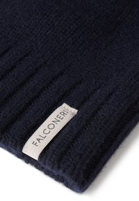 Mörkblått stickat tyg med en ribbad textur; har en framträdande etikett med "FALCONERI" i ljusbeige. Mjuk och varm look.
