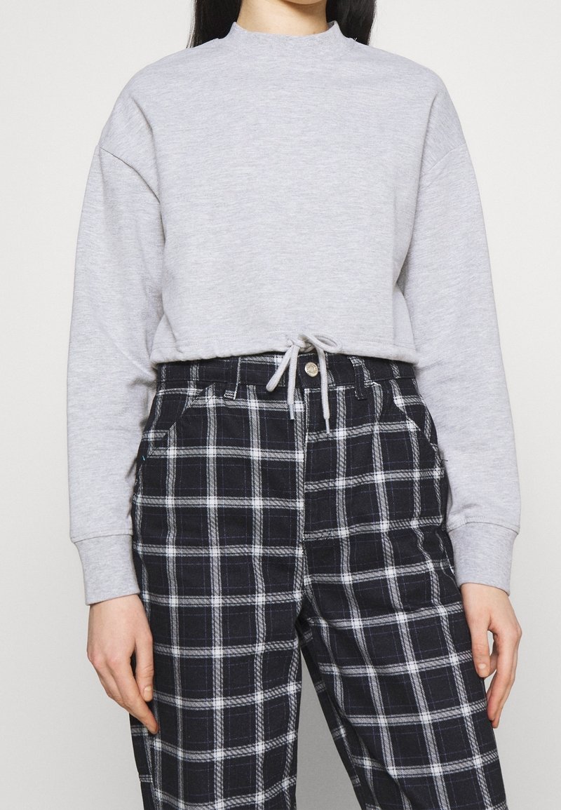 Sudadera de cuello redondo en gris claro con hombros caídos y cordón ajustable. Combinada con pantalones de cuadros en blanco y negro de cintura alta.
