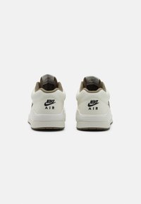 Bílé kožené tenisky s světle hnědými doplňky. Mají polstrovaný límec, texturovaný jazyk a černé logo "Nike Air" na patě.