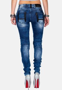 Jeans in denim blu snelli con una finitura sbiadita, dotati di tasche con zip nere e vita intermedia, abbinati a tacchi alti argentati.