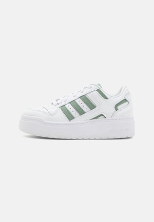 White athletic sneakers with green accents; featuring a textured leather upper, three-striped design, and a thick white rubber sole.