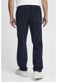 Námornícke manšestrové nohavice s elastickým pásom, jedným zadným vreckom a rovno strihanými nohavicami, v kombinácii s bielymi teniskami.