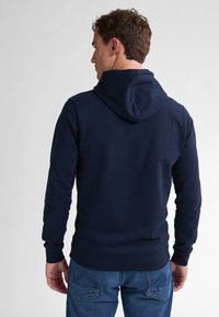 Felpa con cappuccio blu navy con maniche lunghe e polsini a coste, abbinata a jeans blu chiaro. Tessuto morbido e design minimale.