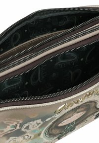 Bolsa con cierre hecha de tela metálica. El interior presenta dos compartimentos con forros contrastantes y patrones de texto impresos. Acentos decorativos visibles.