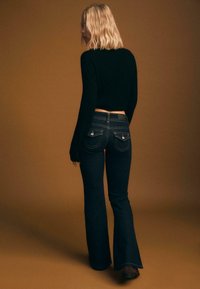 Rozšírené tmavé džínsové nohavice s vysokým pásom, s dvoma zadnými vreckami s dekoratívnym prešívaním a hladkým povrchom. Čierny krátky sveter.
