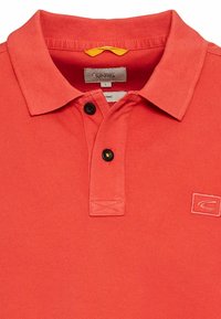 Koralfarvet polo shirt lavet af bomuld; har en foldet krave, to sorte knapper og et lille broderet logo på brystet.
