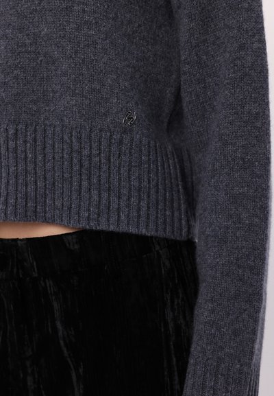 Pull en tricot gris avec un ourlet et des poignets côtelés. Présente un discret logo sur le devant. Associe avec un pantalon en tissu texturé noir.