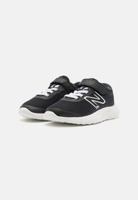 Chaussures de sport en mesh noir avec accents blancs, dotées d'une sangle à crochets et d'un laçage, et d'une semelle blanche rembourrée.