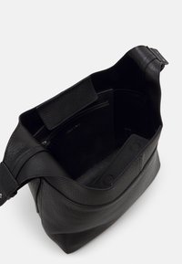 Bolso de mano de cuero negro con acabado texturizado, cierre magnético, bolsillo interior con cremallera y una correa ancha y suave para un transporte cómodo.