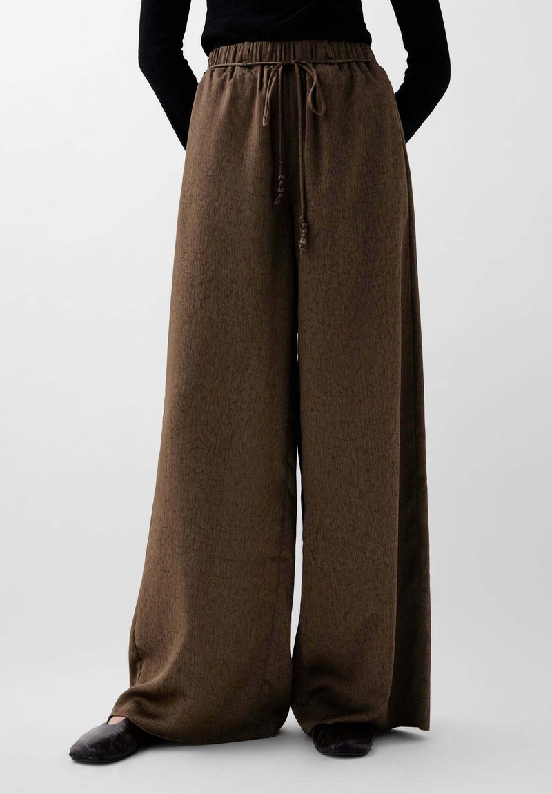 Braune weit geschnittene Hose aus strukturiertem Stoff, mit elastischem Bund und Kordelzug mit dekorativen Quasten, lässig gestylt.