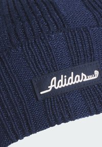 Granatowa dzianinowa czapka z prążkowaną fakturą i prostokątną czarną naszywką z napisem „Adidas Golf” w białych literach.