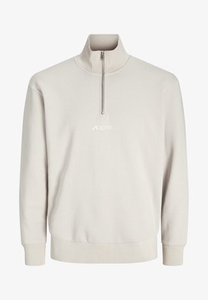 Beige langærmet pullover med ribstrikkede ærmekanter og kant, en kvart lynlås foran ved kraven, samt et lille centreret logo under lynlåsen.