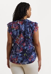 Blomstermønstret bluse i blå, rød og grønnyanser, med volang korte ermer og avrundet nederkant. Lett, teksturert stoff.