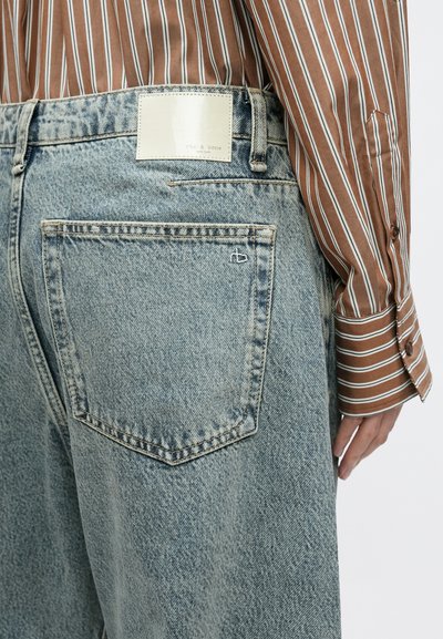 Heledad ja helesinise tooniga teksapüksid, millel on nähtav tagatasku, nahkmärgiga brändinimega ja mugava lõikega. Näha on triibuline särk.