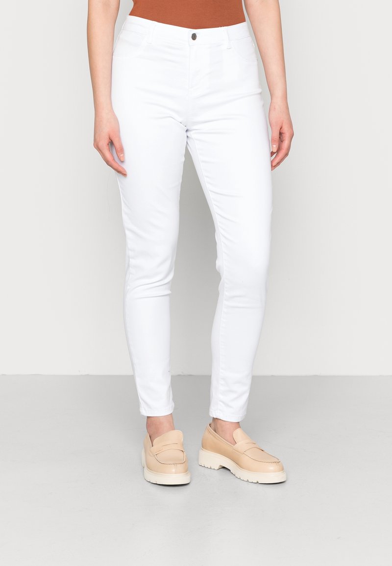 Witte nauwsluitende jeans met een middelhoge taille, voorzien van voorzakken en een enkele knoopsluiting. Gecombineerd met lichtbeige instappers.