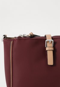 Geantă din nylon burgund cu o textură netedă, prezentând un fermoar argintiu, accente din piele bej și un detaliu contrastant de margine maro.