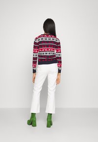 Röd och marinblå mönstrad tröja med snöflingor och renar, matchad med vita byxor och gröna mockaboots med klack.