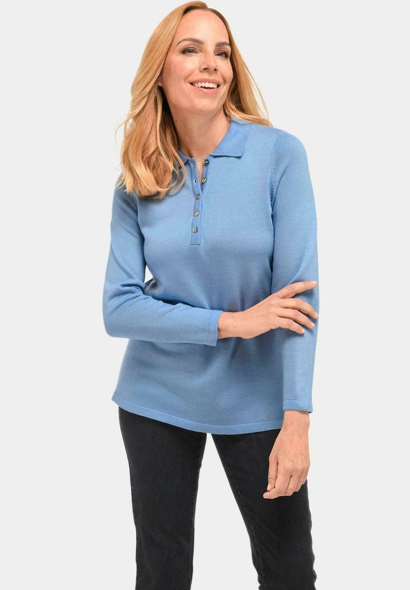 Lichtblauwe lange mouwen polo-shirt met een knoopjessluiting en geribbelde textuur. Gekleed met donkere jeans.