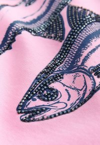 Lichtroze stof met een donkerblauw visontwerp omlijnd met kleine kralen. Heeft een gladde textuur en fijne kralenbewerking.