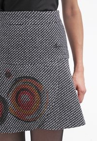Jupe en tweed noir et blanc présentant un motif abstrait de tourbillon multicolore, avec une taille cintrée et un ourlet évasé. La texture semble tissée.