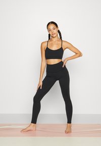 Mustat urheiluvaatteet, joissa on istuva urheiluliivi ohuilla olkaimilla ja korkeavyötäröiset legginsit. Sujuva, joustava materiaali, jossa on tasaiset saumat.