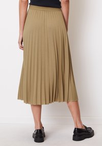 Jupe midi plissée en vert olive, dotée d'une large taille élastique et d'un tissu fluide. Portée avec des chaussures noires chunky.