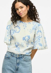 Blusa a stampa floreale in tessuto leggero, con fiori blu su sfondo crema, maniche a sbuffo corte e scollatura rotonda.