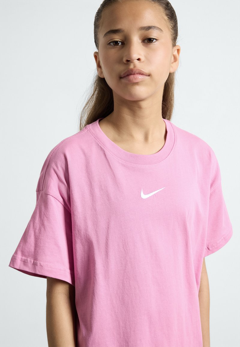 Růžové bavlněné tričko s krátkými rukávy, na hrudi s bílým logem Nike swoosh. Měkká textura a volný střih s kulatým výstřihem.